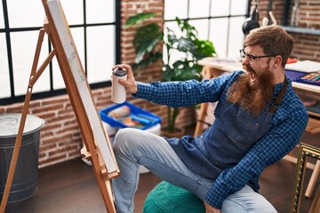 Young redhead man artist smiling confident using graffiti spray drawing at art studio