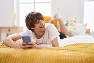 Young blond man using smartphone lying on bed at bedroom