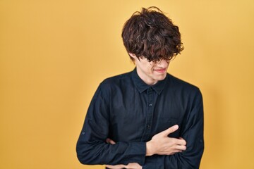 Obraz premium Young man wearing glasses over yellow background with hand on stomach because nausea, painful disease feeling unwell. ache concept.