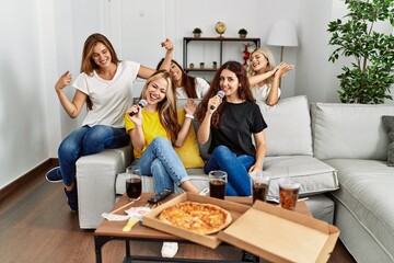 Group of young woman friends having party eating italian pizza and singing song at home.