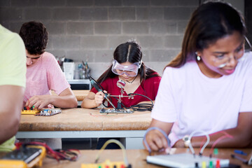 A group of technical college students are in the classroom studying, practicing soldering pieces of...