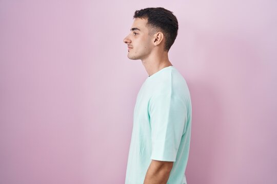 Handsome hispanic man standing over pink background looking to side, relax profile pose with natural face and confident smile.