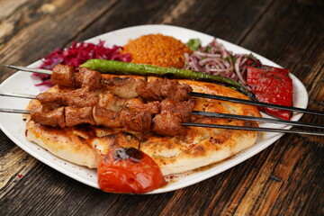 Beef shish kebabs with onion, rice, and tomatoes in a white bowl on wooden background. Traditionally marinated beef shish kebab. Traditional grilled kebabs.