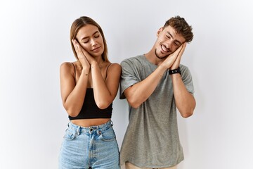 Naklejka premium Young beautiful couple standing together over isolated background sleeping tired dreaming and posing with hands together while smiling with closed eyes.