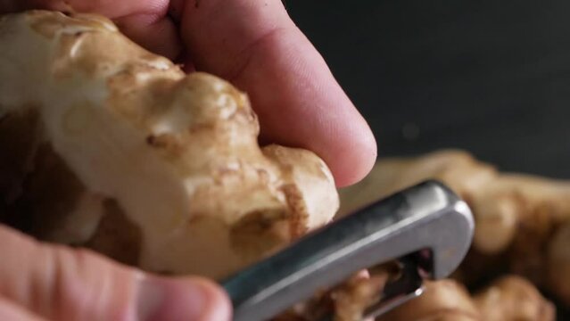 Chef peeling raw fresh jerusalem artichokes or ginger close up.