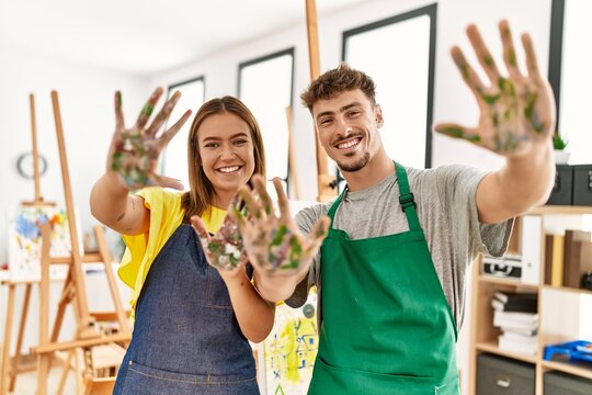 Young hispanic artist couple smiling happy showing painted palm hands at art studio.