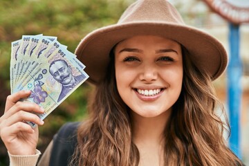 Young hispanic tourist woman smiling happy holding romania lei banknotes at the city.