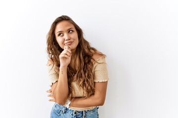 Beautiful hispanic woman standing over isolated while background with hand on chin thinking about question, pensive expression. smiling with thoughtful face. doubt concept.