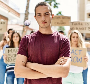 Young activist man with arms crossed gesture standing with a group of protesters holding banner protesting at the city.