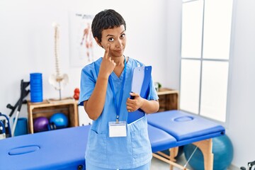 Young hispanic woman with short hair working at pain recovery clinic pointing to the eye watching you gesture, suspicious expression