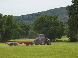 Tractor pulling a long trailer which will be used to transport bales of hay in a meadow in the Alpilles in Provence in France 