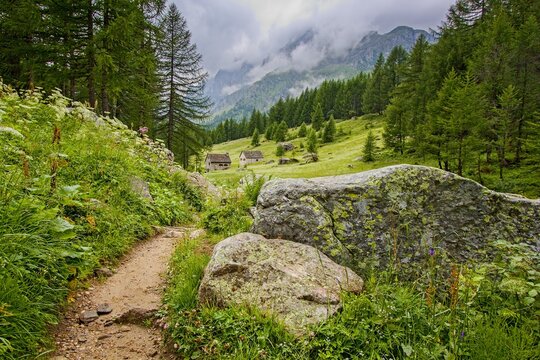 Tourist trail between Crampiolo and Catone with a view of stone houses and mountains in mist, Alpe Devero, Lepontine Alps, Ossola, Piedmont, Italy