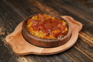 Delicious Fried eggs with pastrami inside in a casserole on wooden background. Fried eggs with pastrami made with butter. 