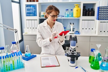 Young caucasian woman wearing scientist uniform using touchpad working at laboratory