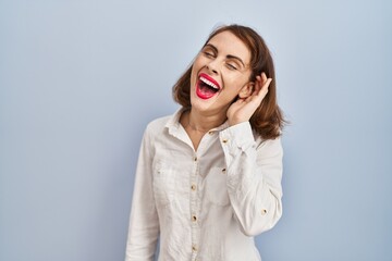 Young beautiful woman standing casual over blue background smiling with hand over ear listening an hearing to rumor or gossip. deafness concept.