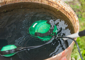 a submersible pump with an attached hose for pumping water is immersed in a metal barrel with water.