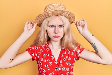 Beautiful caucasian woman with blond hair wearing summer hat skeptic and nervous, frowning upset...