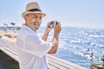 Senior man smiling confident wearing summer hat using camera at seaside