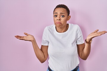 Beautiful african american woman standing over pink background clueless and confused expression...