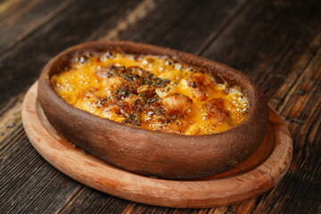 Potato gratin in the casserole on wooden background. Potato gratin made with baked potatoes, cream, cheese and rosemary. Delicious appetizer. 