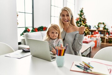 Mother of caucasian daughter wearing call center agent headset at home screaming proud, celebrating victory and success very excited with raised arms