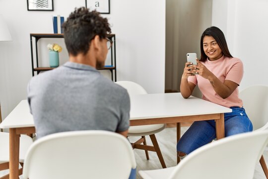 Young latin woman making man picture using smartphone at home.
