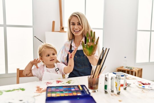 Mother and daughter smiling confident painting palm hands at art studio