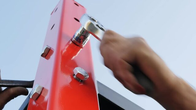 looking up: the installer's hands are tightening the nut with a ratchet wrench. The process of assembling a metal structure from iron beams. Outdoor sports equipment