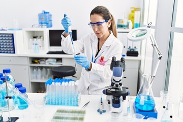 Young hispanic woman wearing scientist uniform using pipette at laboratory