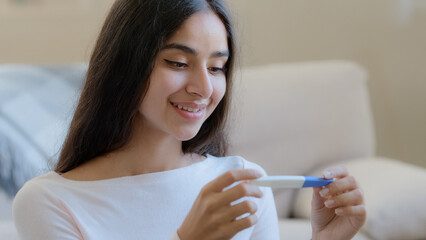 Portrait of joyful happy pregnant woman future mom sits at home holds pregnancy positive test result. Beautiful arabian latino young housewife expecting baby anticipate childbirth planning parenthood