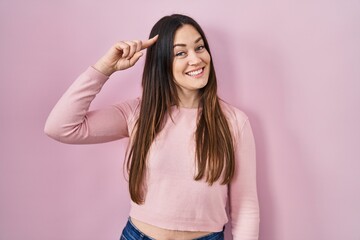 Young brunette woman standing over pink background smiling pointing to head with one finger, great idea or thought, good memory