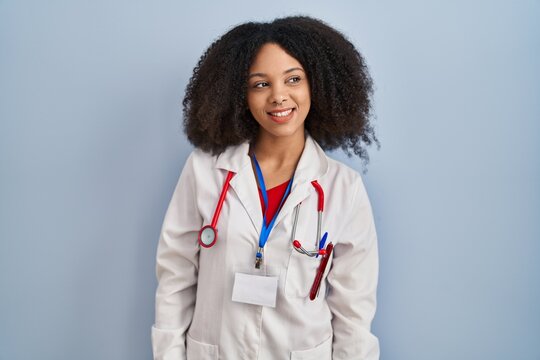 Young african american woman wearing doctor uniform and stethoscope looking away to side with smile on face, natural expression. laughing confident.
