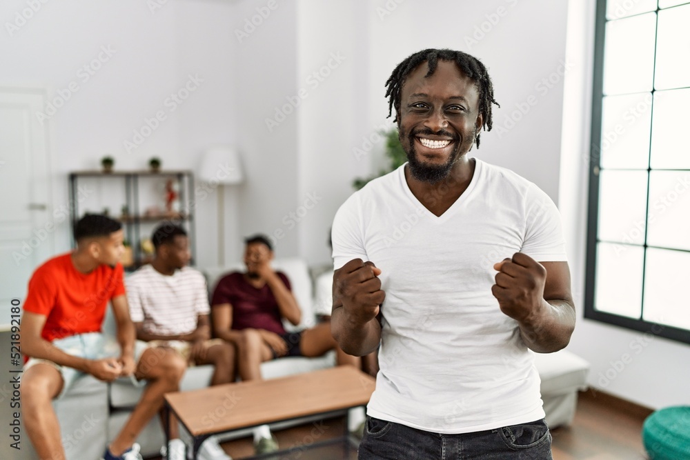 Sticker Young african man with friends at the living room very happy and excited doing winner gesture with arms raised, smiling and screaming for success. celebration concept.