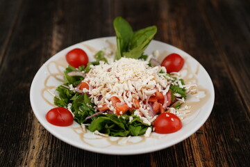 Salad mix with tomato, cucumber, olive oil, onion slices, and grated cheese in a bowl on a wooden table. Healthy food. Vegetarian food. 