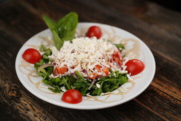 Salad mix with tomato, cucumber, olive oil, onion slices, and grated cheese in a bowl on a wooden table. Healthy food. Vegetarian food. 