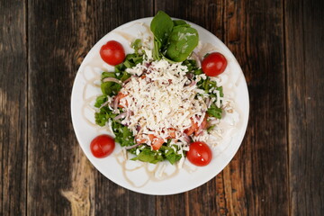 Salad mix with tomato, cucumber, olive oil, onion slices, and grated cheese in a bowl on a wooden table. Healthy food. Vegetarian food. 