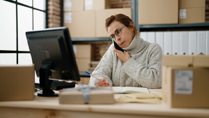Middle age hispanic woman ecommerce business worker talking on the smartphone at storehouse office