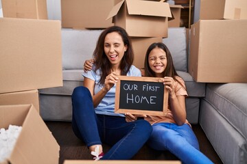 Young mother and daughter sitting on the floor at new home winking looking at the camera with sexy...