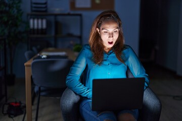 Brunette woman working at the office at night afraid and shocked with surprise expression, fear and excited face.