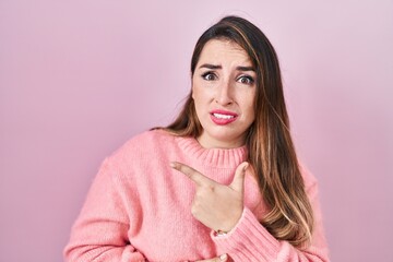 Young hispanic woman standing over pink background pointing aside worried and nervous with...