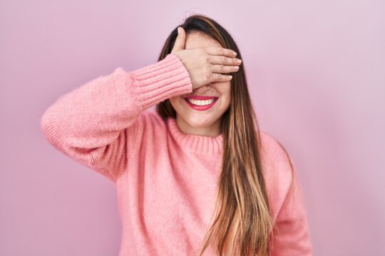 Young hispanic woman standing over pink background smiling and laughing with hand on face covering eyes for surprise. blind concept.