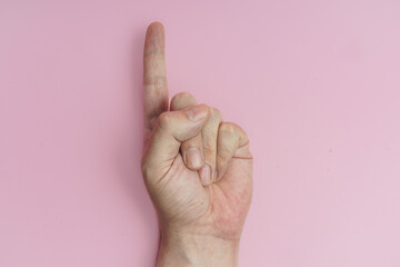 Mano haciendo gesto de numero uno, primero,  sobre fondo rosa.