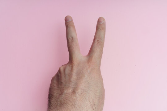Mano haciendo gesto de 2 dedos sobre fondo rosa.
