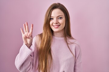 Young caucasian woman standing over pink background showing and pointing up with fingers number four while smiling confident and happy.