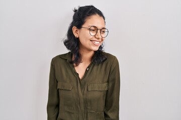 Hispanic woman with dark hair standing over isolated background looking away to side with smile on face, natural expression. laughing confident.