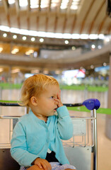 baby at the airport departures terminal patiently sits in the luggage cart.