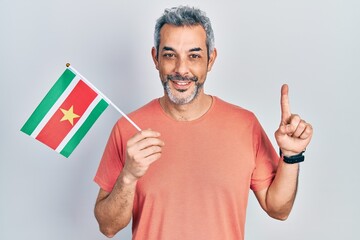 Handsome middle age man with grey hair holding suriname flag smiling with an idea or question...