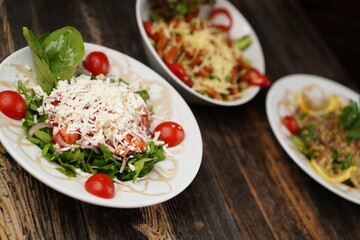 Different types of mixed salad with tomato, cucumber, olive oil, onion slices, and grated cheese in a bowl on a wooden table. Healthy food. Vegetarian food.  