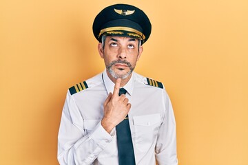 Handsome middle age man with grey hair wearing airplane pilot uniform thinking concentrated about...