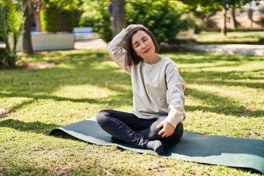 Middle age woman smiling confident stretching head at park